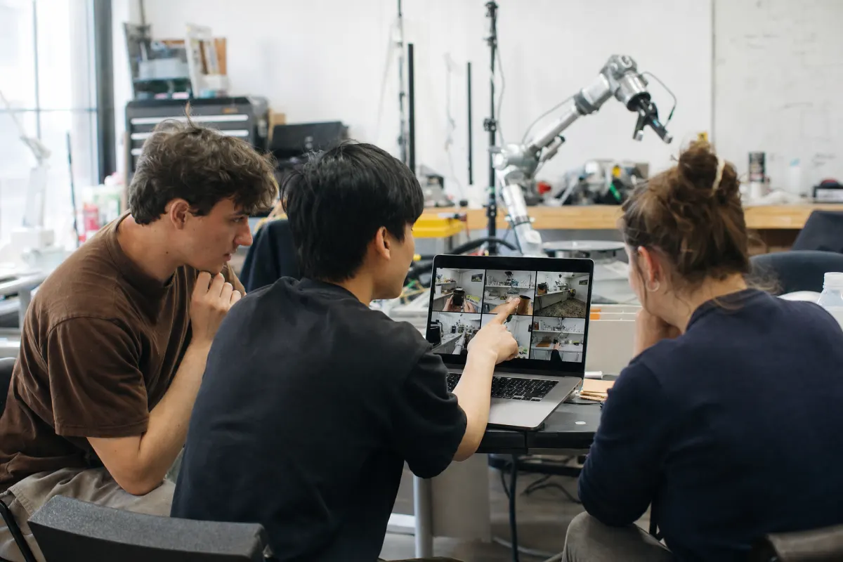 A robotics team reviews a grid of first-person kitchen clips on a laptop